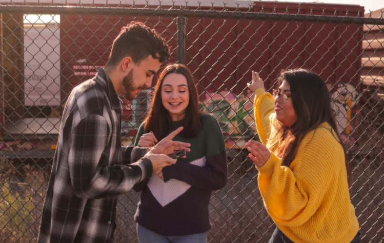 One make and two female teenagers smiling and laughing while the male uses a phone